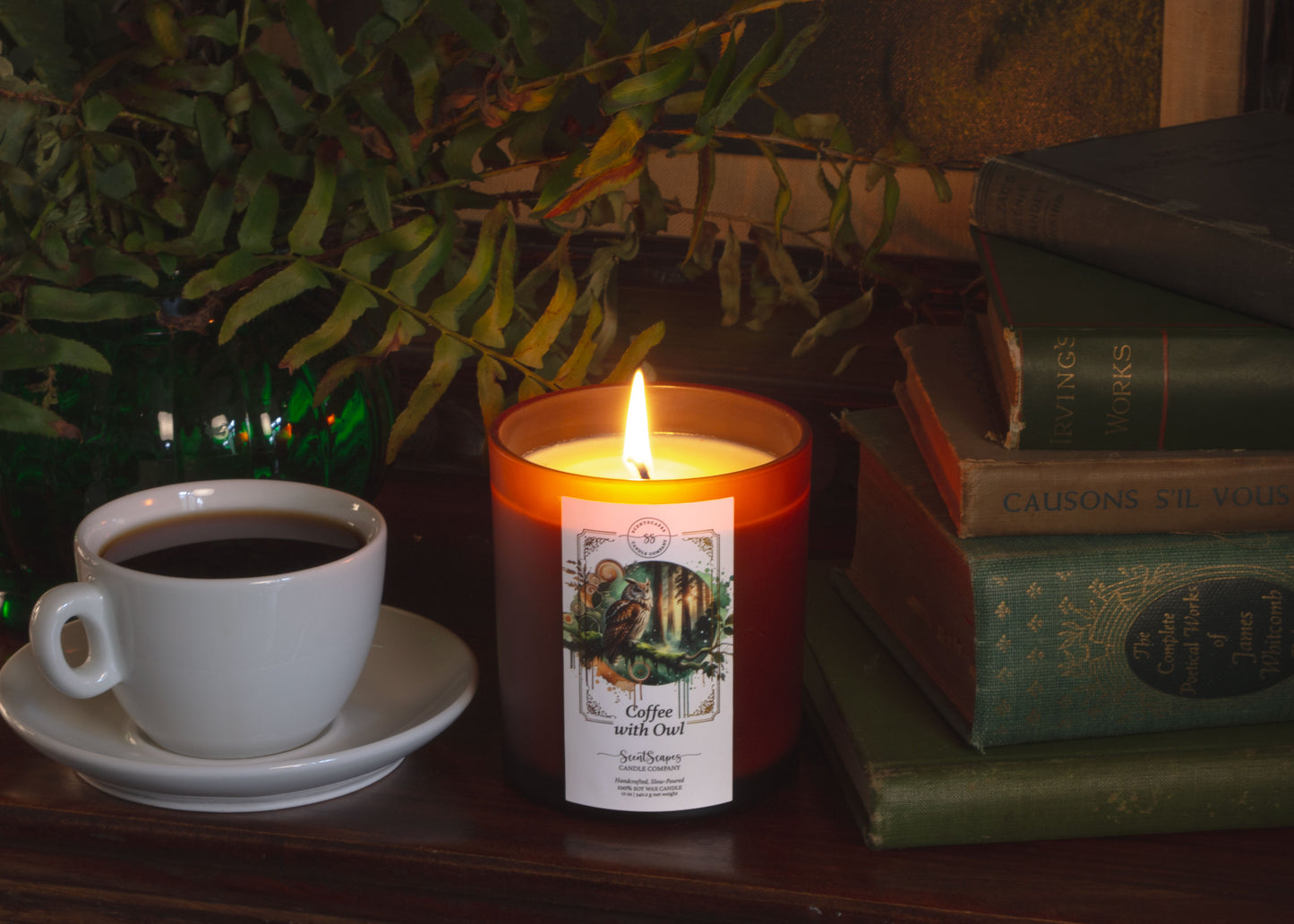A lit ScentScapes candle with a label featuring an owl, placed in a natural setting with trees and moss in the background. Candle setting includes ferns, old books and a cup of coffee ontop of a wooden table.