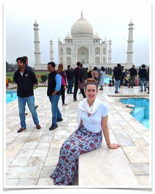 owner and candlemaker of ScentScapes Candle Company sits on white marble bench in front of Taj Mahal in India