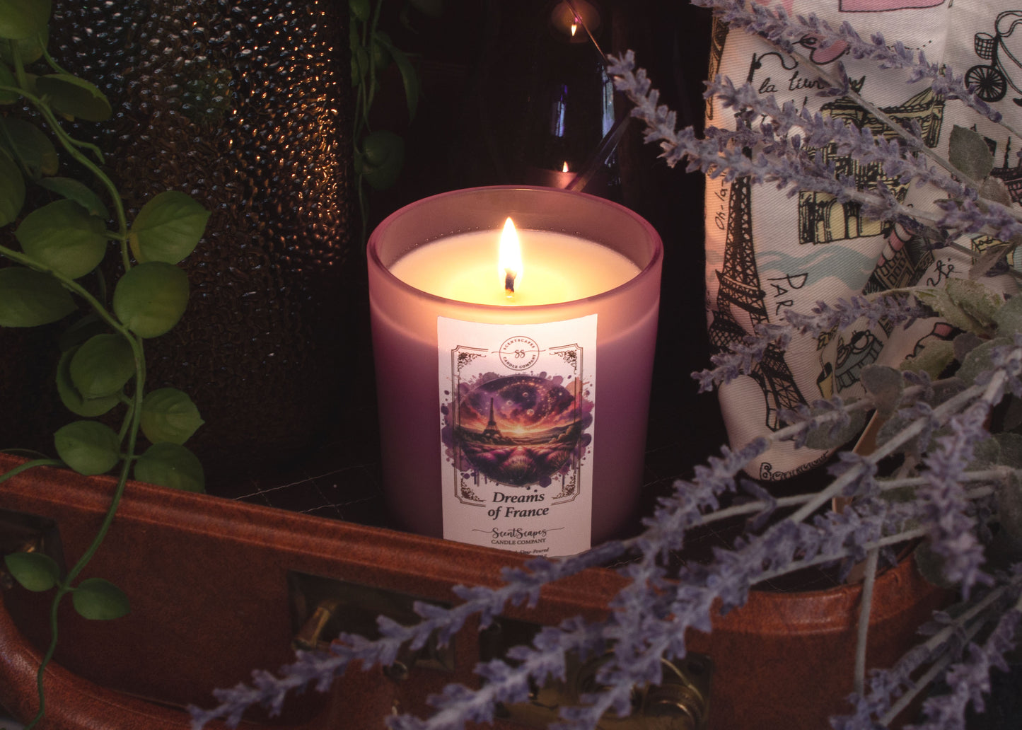 A lit ScentScapes candle in a purple jar with a cork lid, labeled 'Dreams of France' with an image of a glittering the Eiffel Tower and lavender fields.