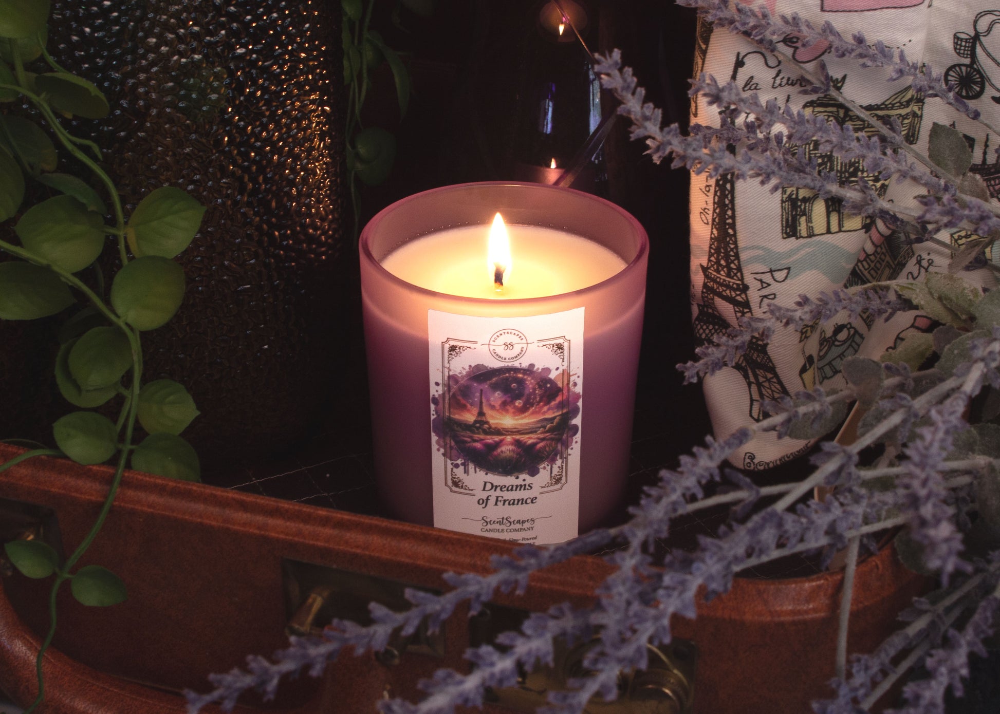 A lit ScentScapes candle in a purple jar with a cork lid, labeled 'Dreams of France' with an image of a glittering the Eiffel Tower and lavender fields.